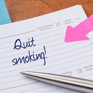 A piece of paper that reads: quit smoking. A pen on the paper with a sticky note, a pink arrow on the paper