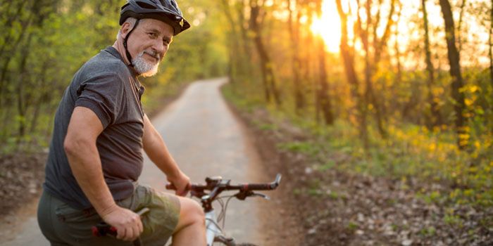 older adult male riding a bicycle down a trail at sunset