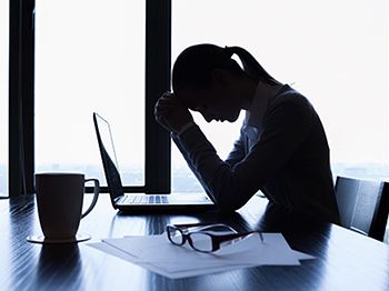 Silhouette of person working at a desk with head in hands